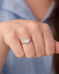Stainless steel silver-tone three-stone ring with aqua blue emerald-cut center stone worn on hand