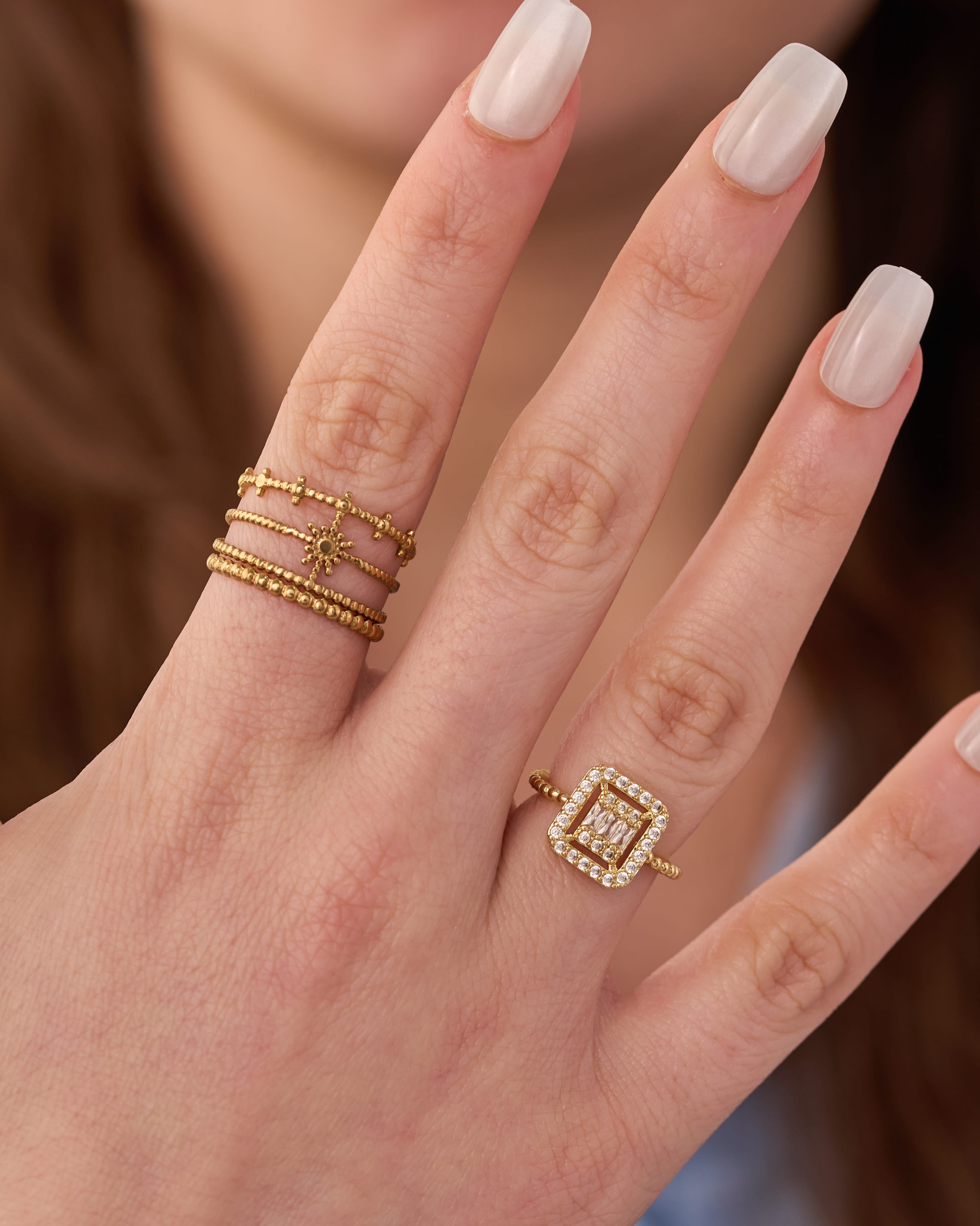 Stainless steel gold-tone stacking rings set with square halo cocktail ring worn on hand