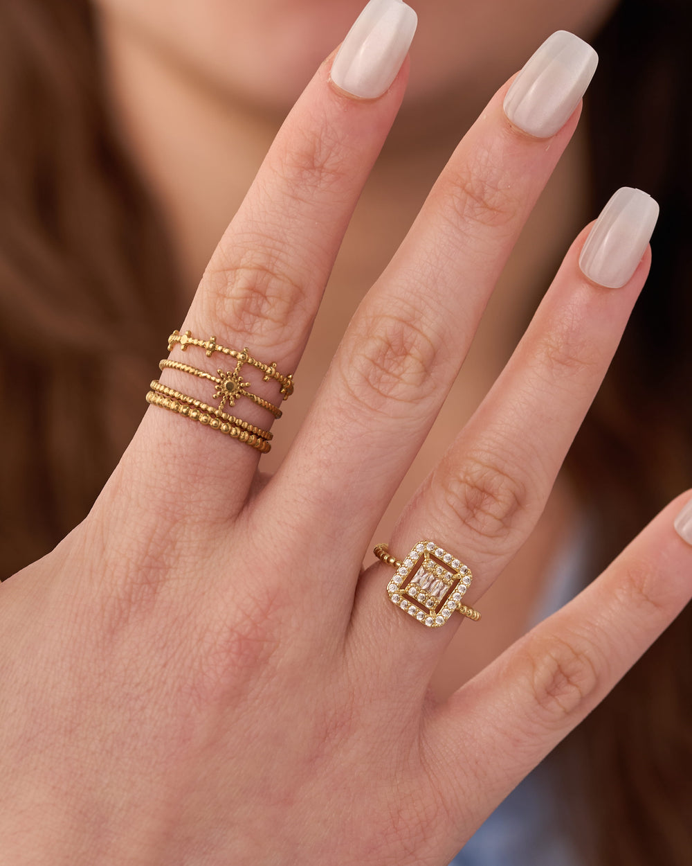 Stainless steel gold-tone stacking rings set with square halo cocktail ring worn on hand
