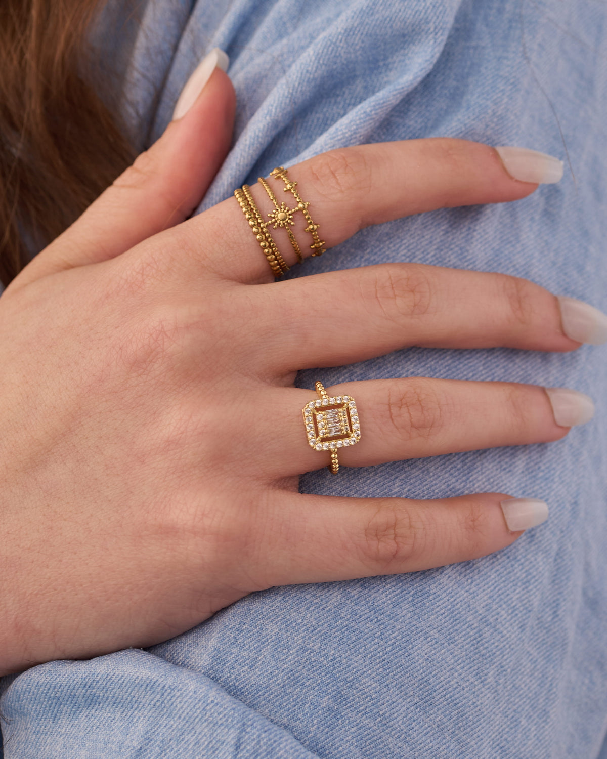 Stainless steel gold-tone stacking rings set with sunburst and square halo designs on hand