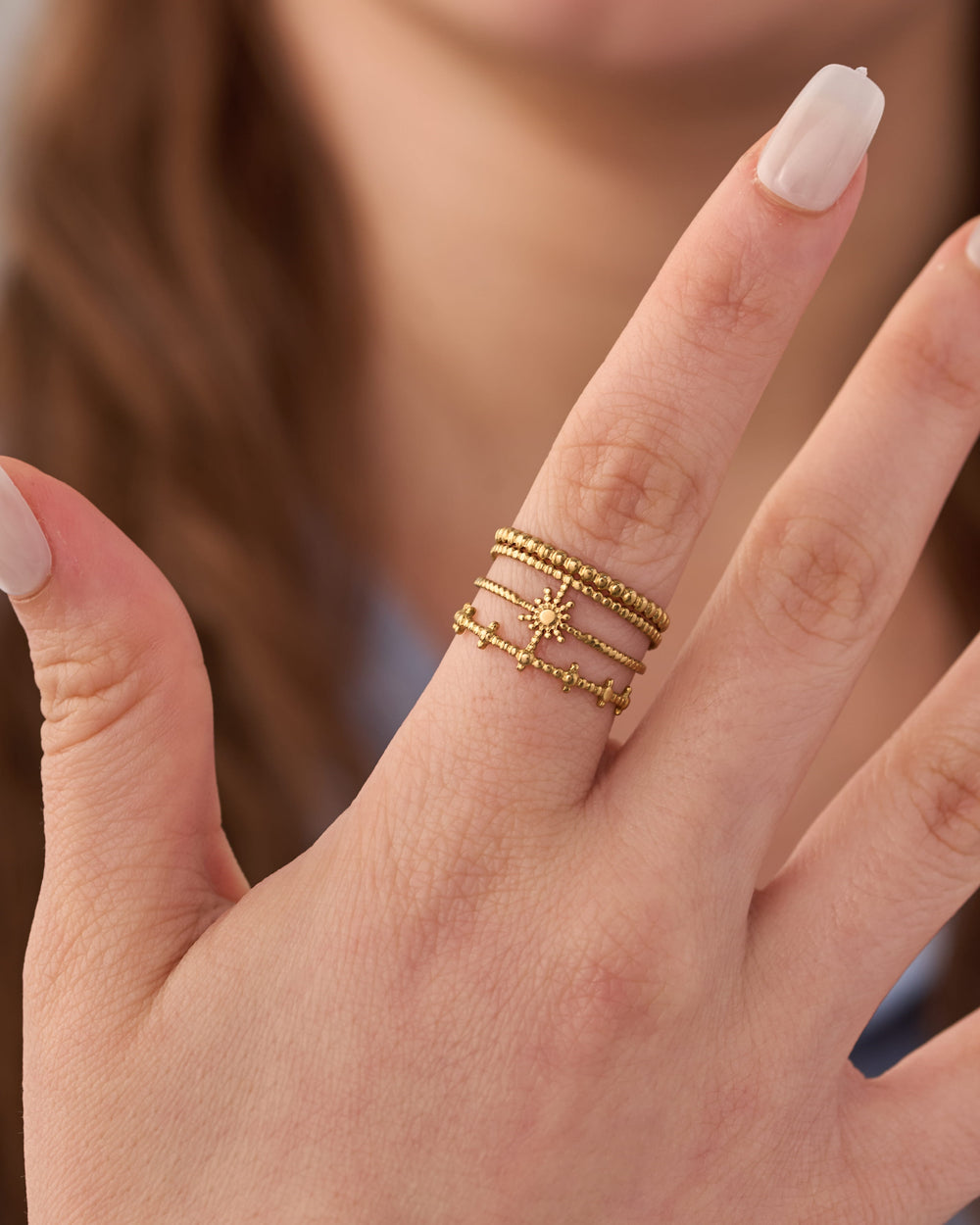 Stainless steel gold-tone beaded stacking rings with starburst detail worn on finger