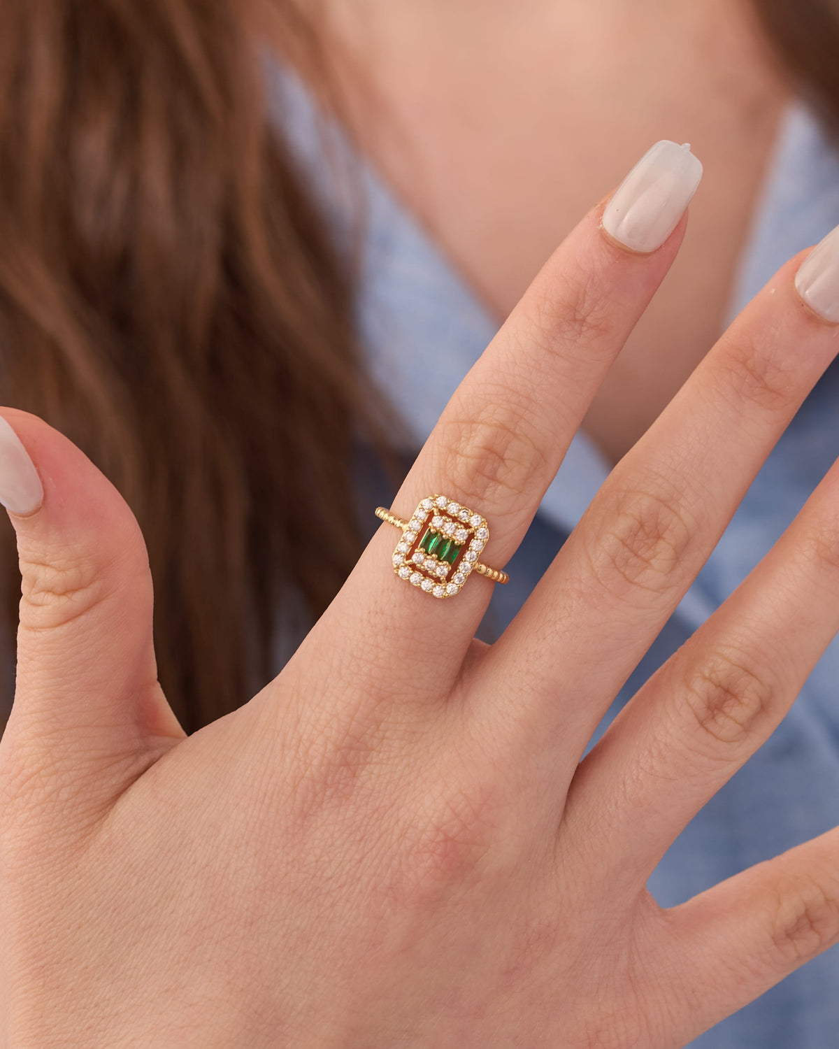 Stainless steel gold-tone square halo cocktail ring with green gemstone center and crystal surround worn on finger