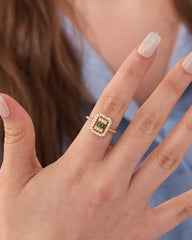 Stainless steel gold-tone square halo cocktail ring with green gemstone center and crystal surround worn on finger