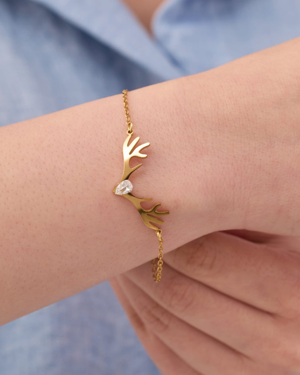 Gold bracelet with a deer design on a wrist against a blue background