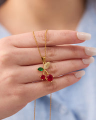 Stainless steel gold-tone cherry pendant necklace with red crystal and green enamel held in hand close-up