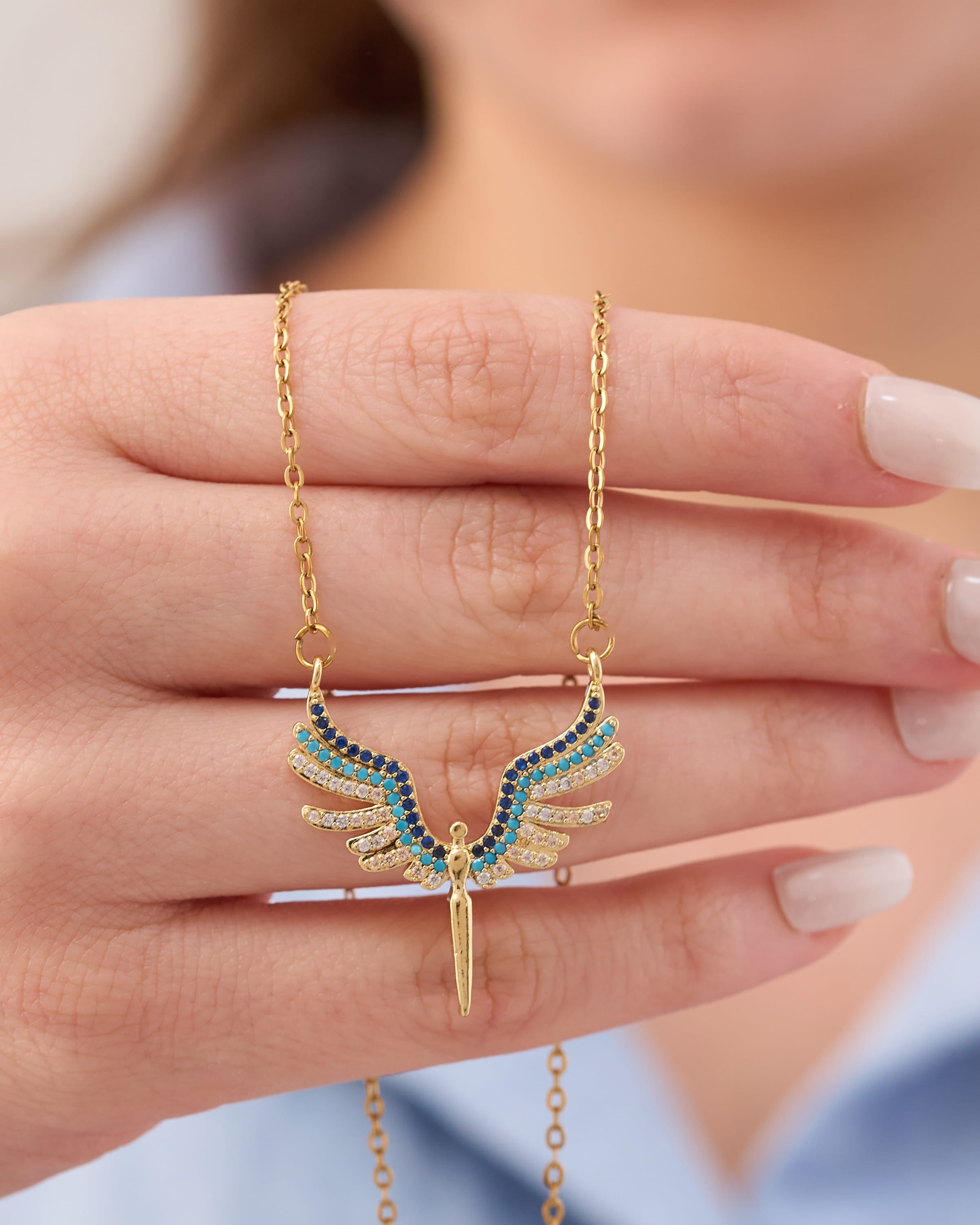 Stainless steel gold-tone angel wings pendant necklace with blue and turquoise crystal stones held in hand