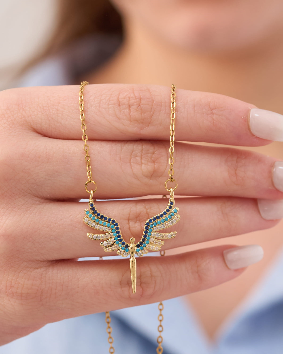 Stainless steel gold-tone angel wings pendant necklace with blue and turquoise crystal stones held in hand