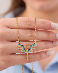 Stainless steel gold-tone angel wings pendant necklace with blue and turquoise crystal stones held in hand