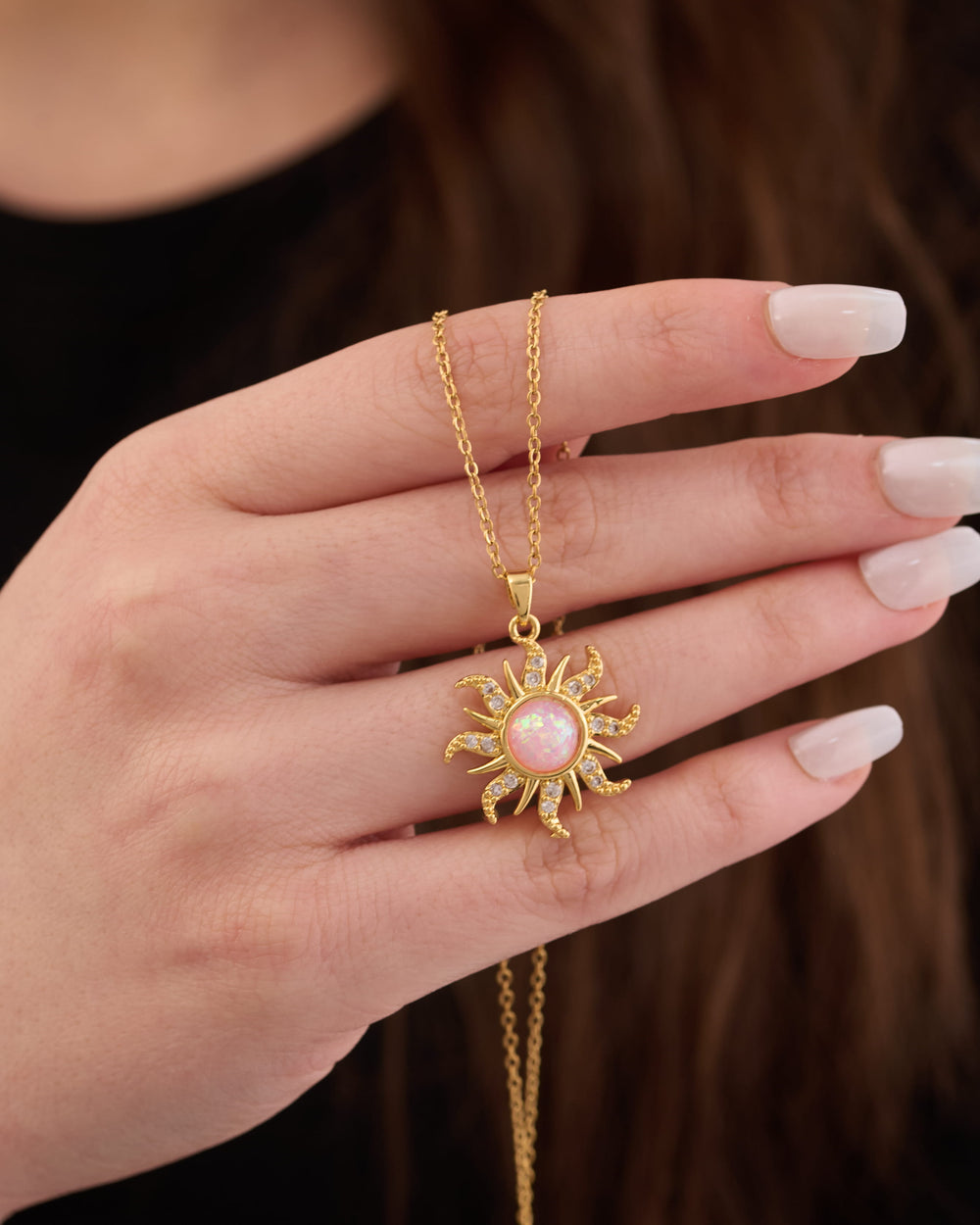 Stainless steel gold-tone sunburst pendant necklace with opal center stone held in hand