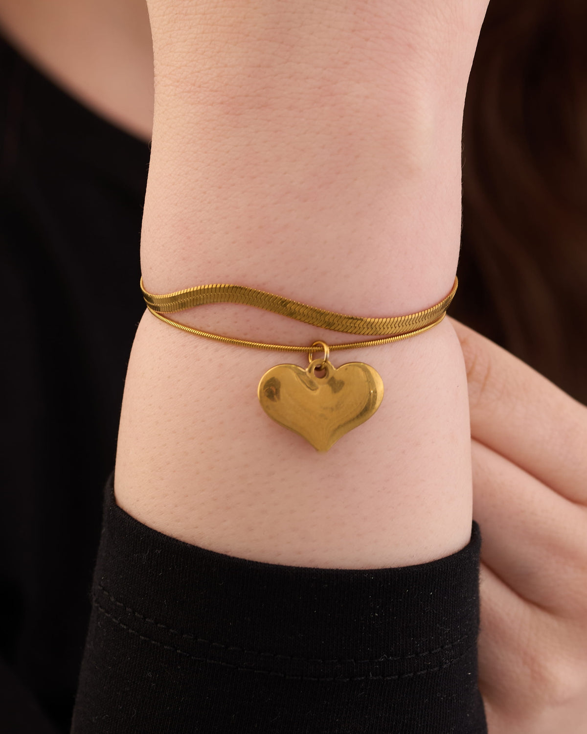 Stainless steel gold-tone herringbone chain bracelet with puffy heart charm on wrist