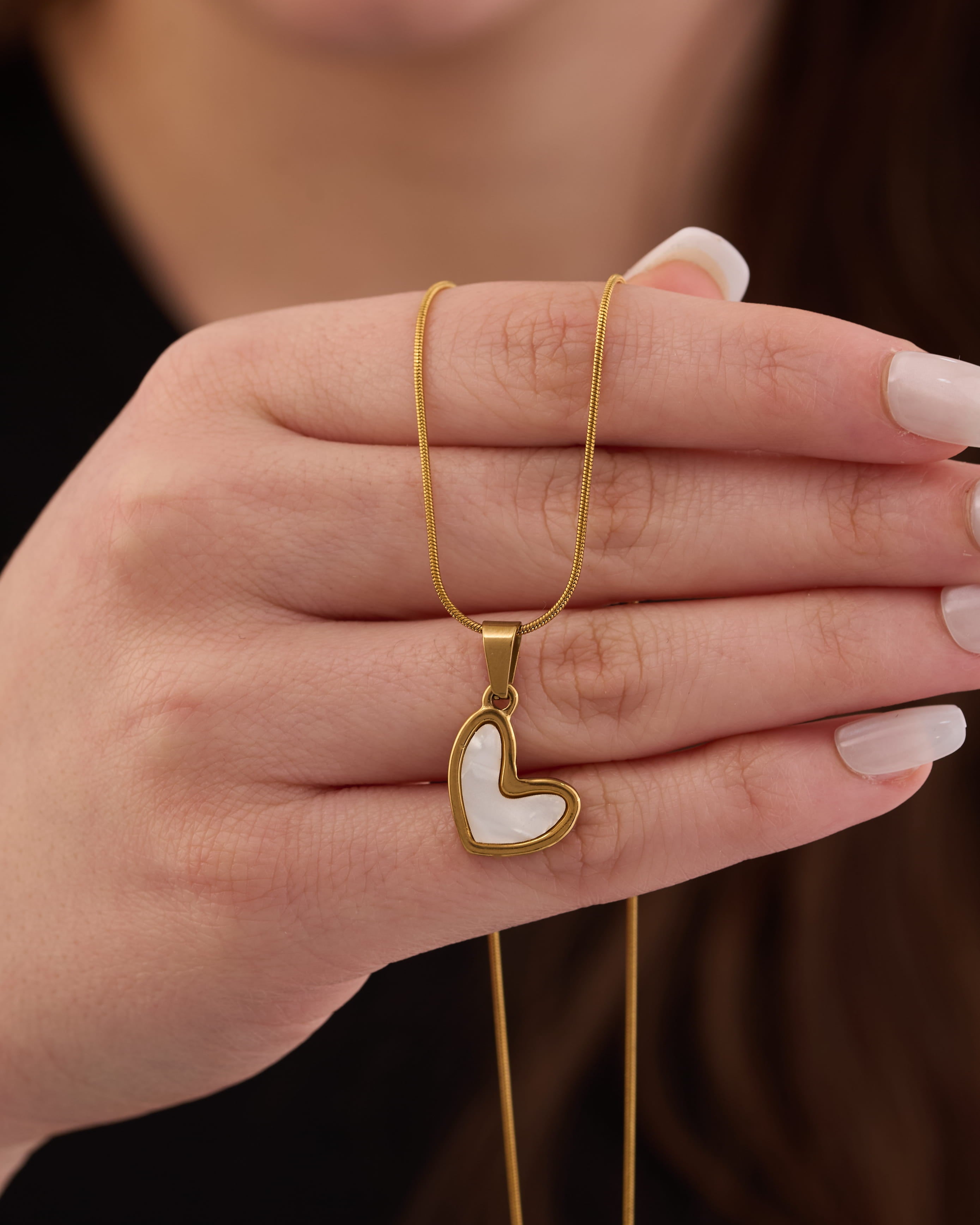 Stainless steel gold-tone heart pendant necklace with white shell inlay held in hand
