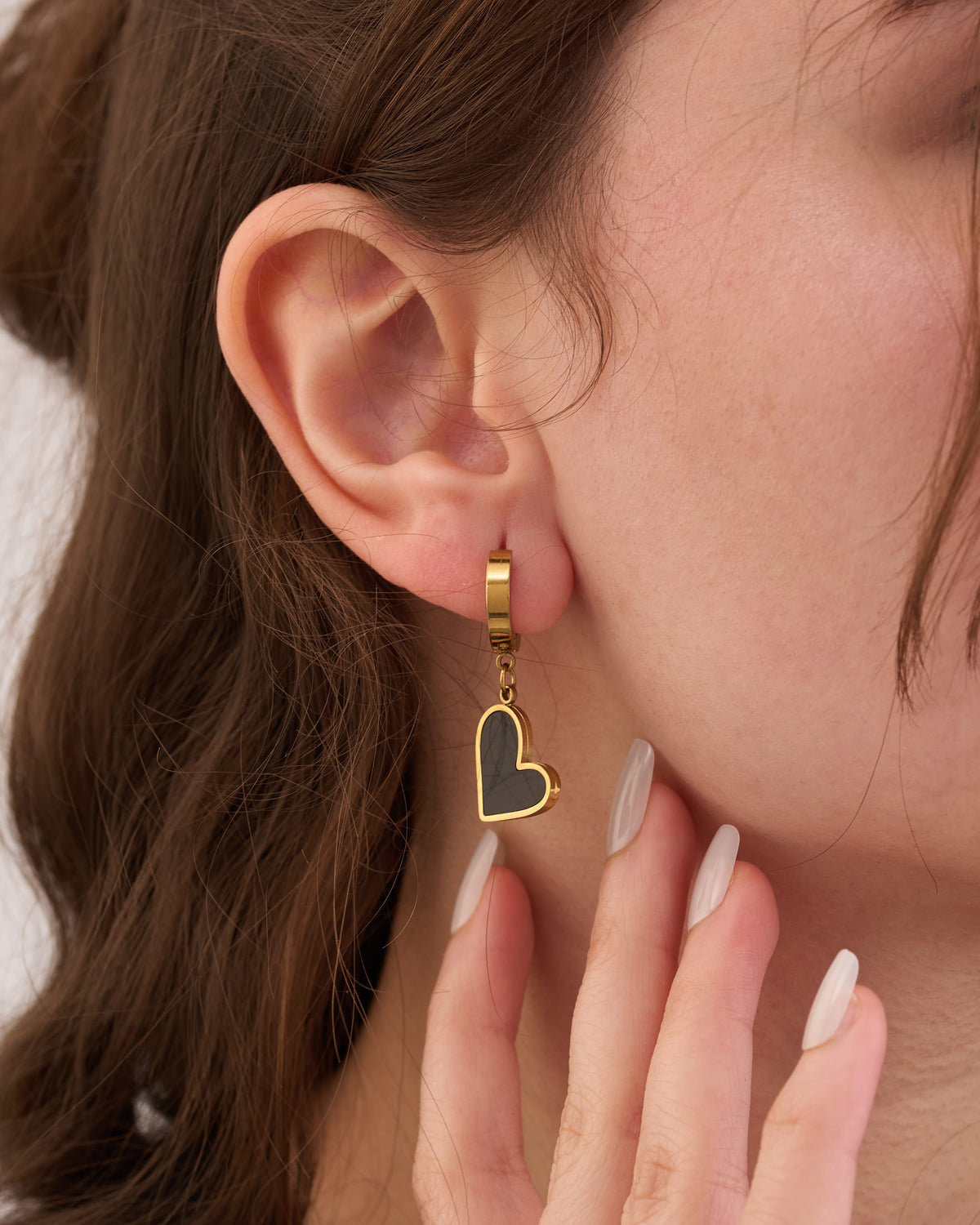 Stainless steel gold-tone huggie hoop earring with dangling open heart charm worn on ear