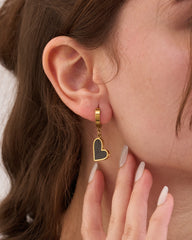 Stainless steel gold-tone huggie hoop earring with dangling open heart charm worn on ear